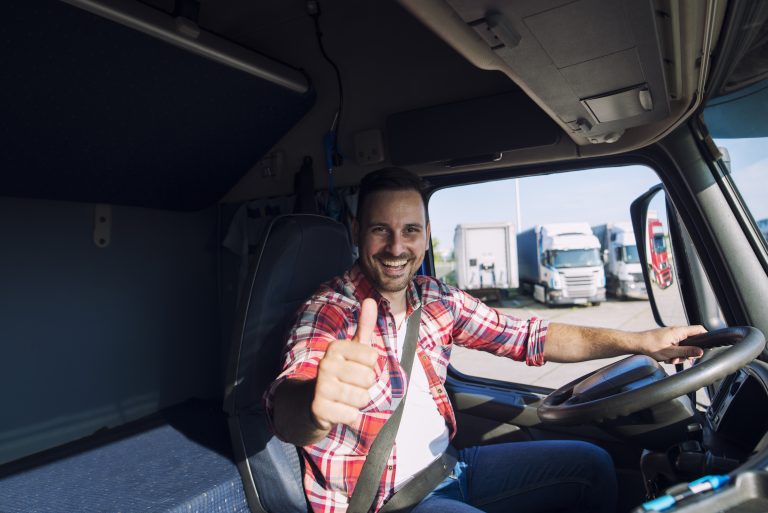 Portrait of professional motivated truck driver holding thumbs up in truck cabin.